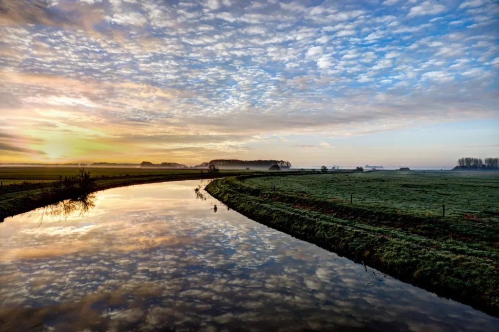 Watergang door een open landschap bij zonsopkomst